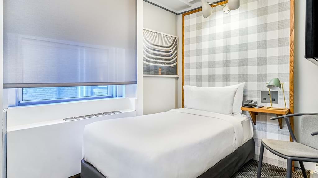 A hotel room with a bed, window, desk, and chair.
