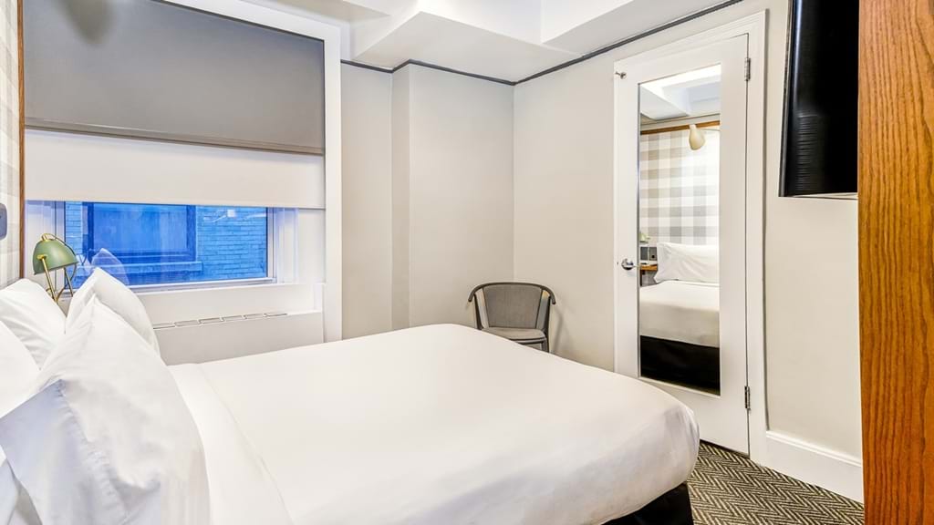 A hotel room with a bed, window, door, and chair.