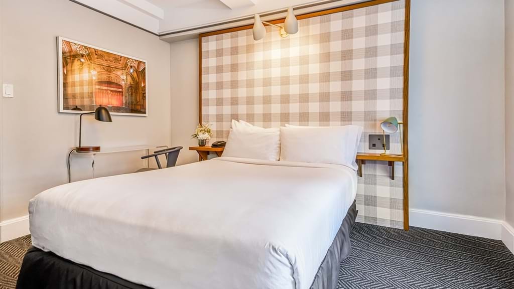 A neatly made hotel room with a large bed, desk, and chair.