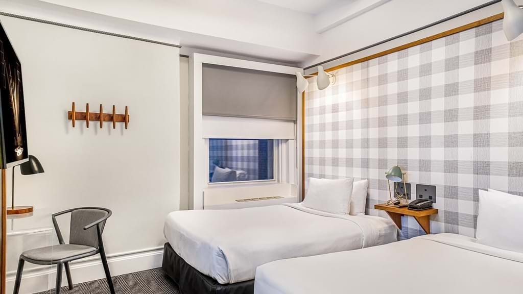 A hotel room with two beds, a window, a chair, a TV, and a phone.